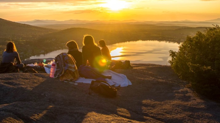 Nuoria/retkeilijöitä kukkulan päälllä, auringonlaskua vasten
