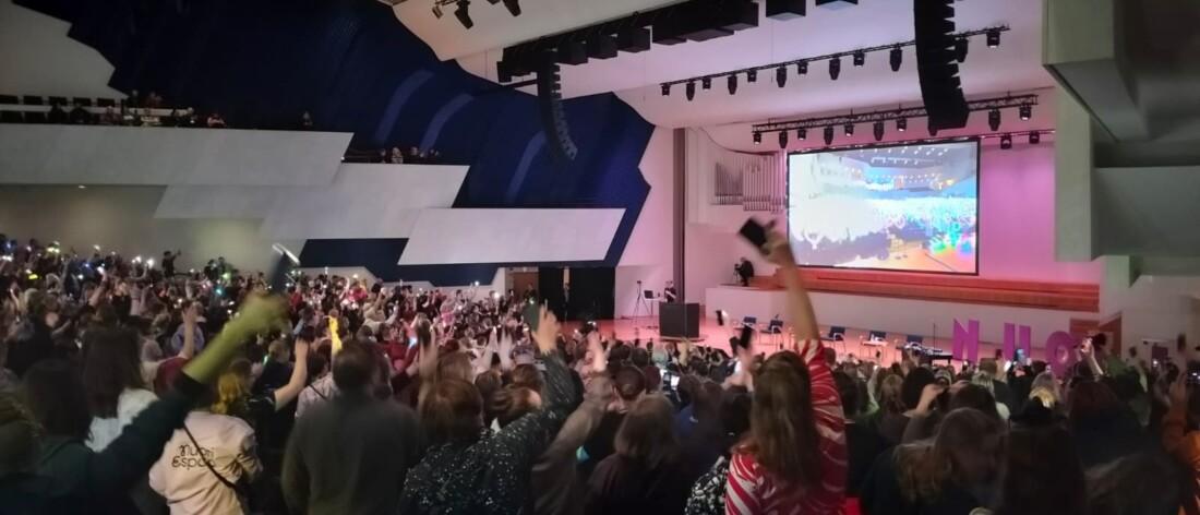 Suuri yleisö juhlii auditoriossa NUORI2026-tapahtumassa heiluttamalla älypuhelimien valoja kohti näyttämöä.
