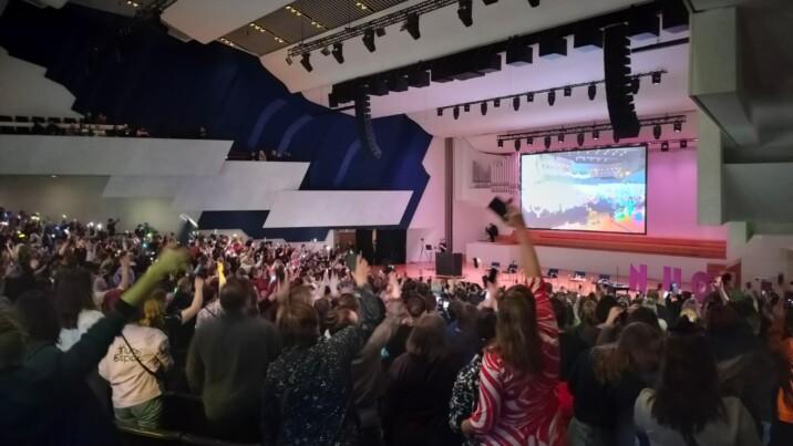 Suuri yleisö juhlii auditoriossa NUORI2026-tapahtumassa heiluttamalla älypuhelimien valoja kohti näyttämöä.