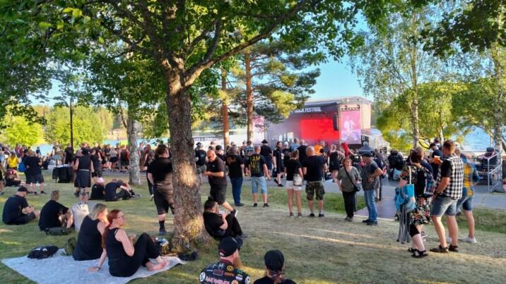 Ihmisjoukko ulkoilmassa John Smith -festareilla nurmikolla puiden alla.